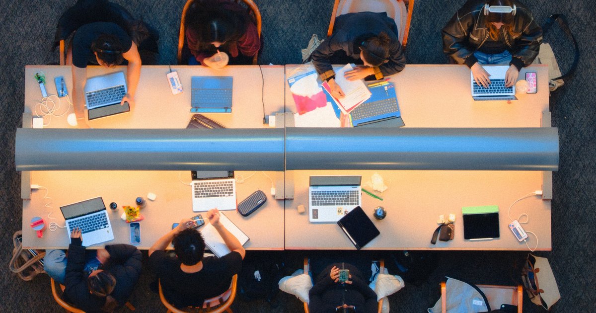 Students working on laptops at long library desks, seen from above