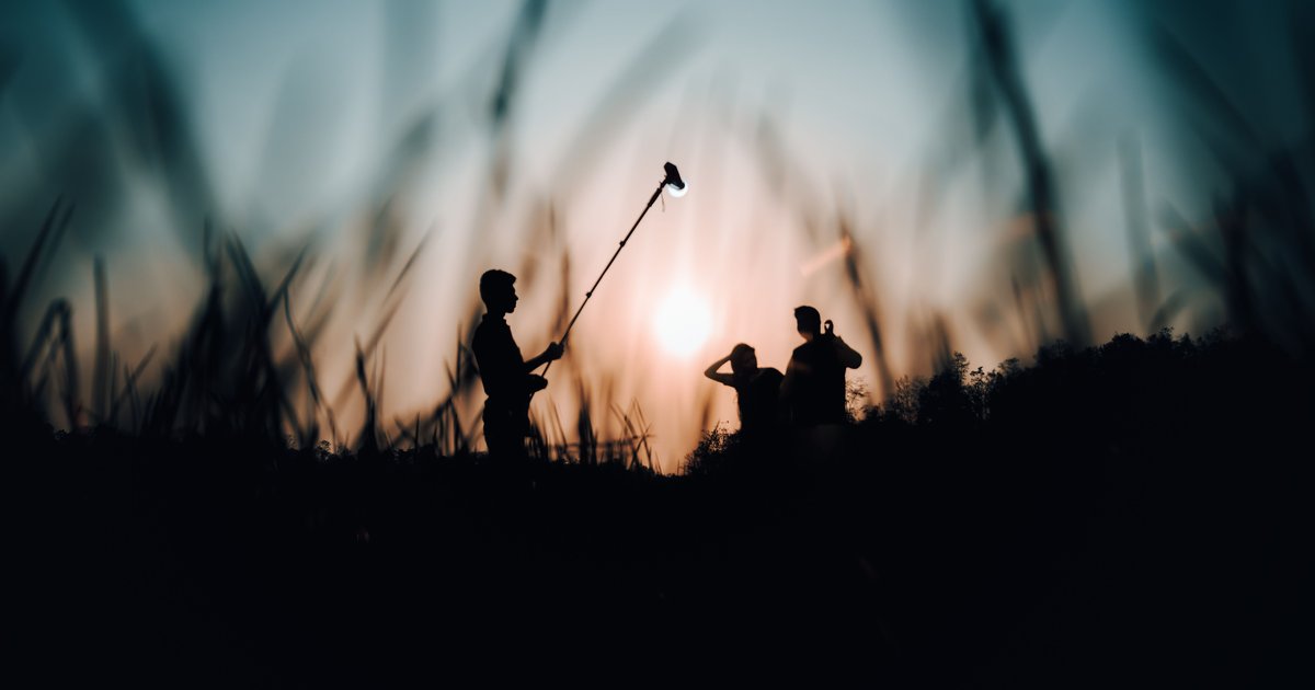 A film crew silhouetted at sunset, one holding a boom microphone