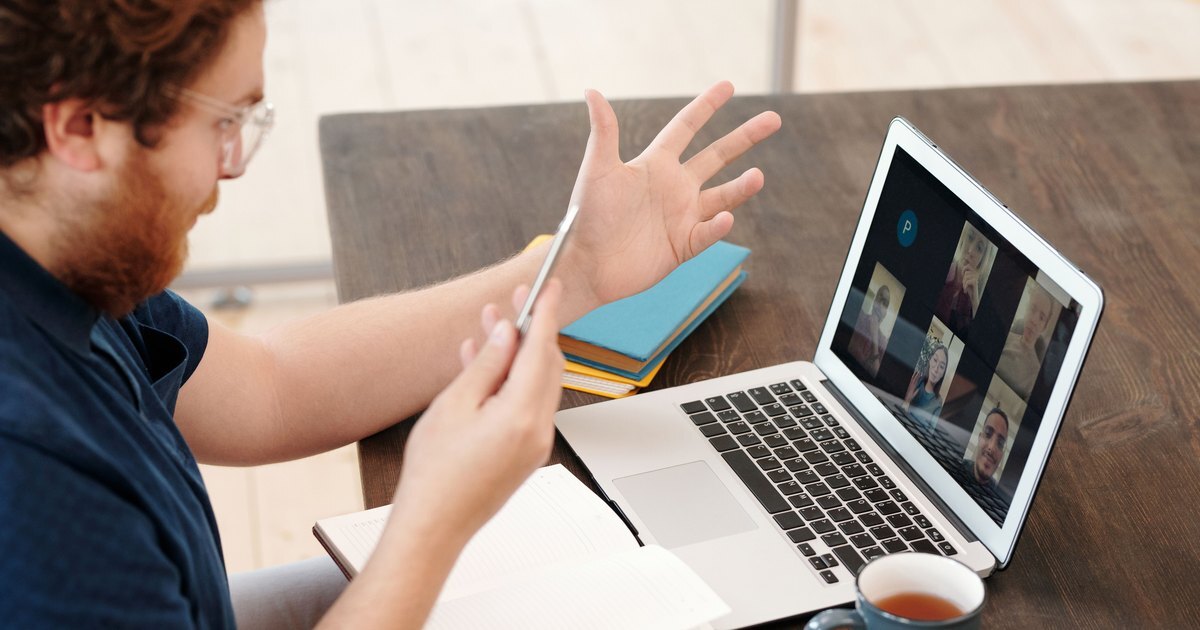 A man gesturing as he talks with a group on a video call on his laptop