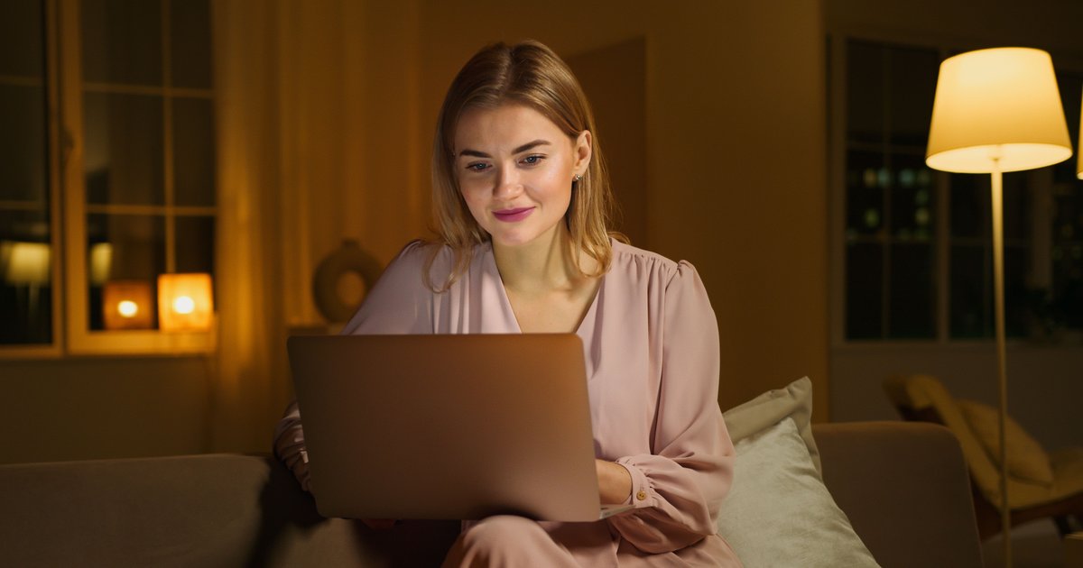 A woman studying on a laptop on her couch in the evening